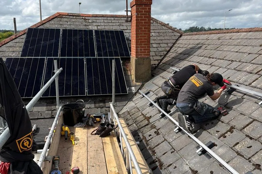 SolarFX installers fitting mounting rails on a tiled roof beside a completed panel array