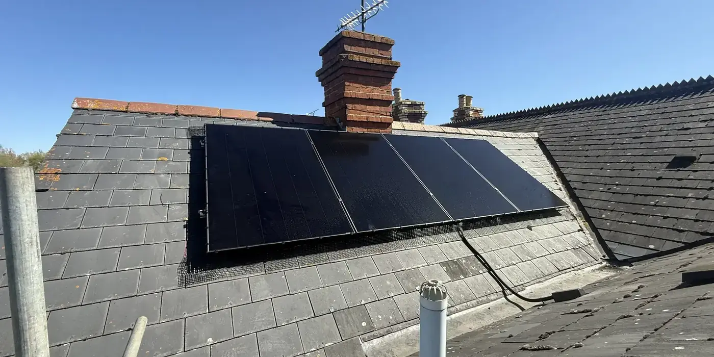 Completed black solar array on a slate roof beside a chimney stack
